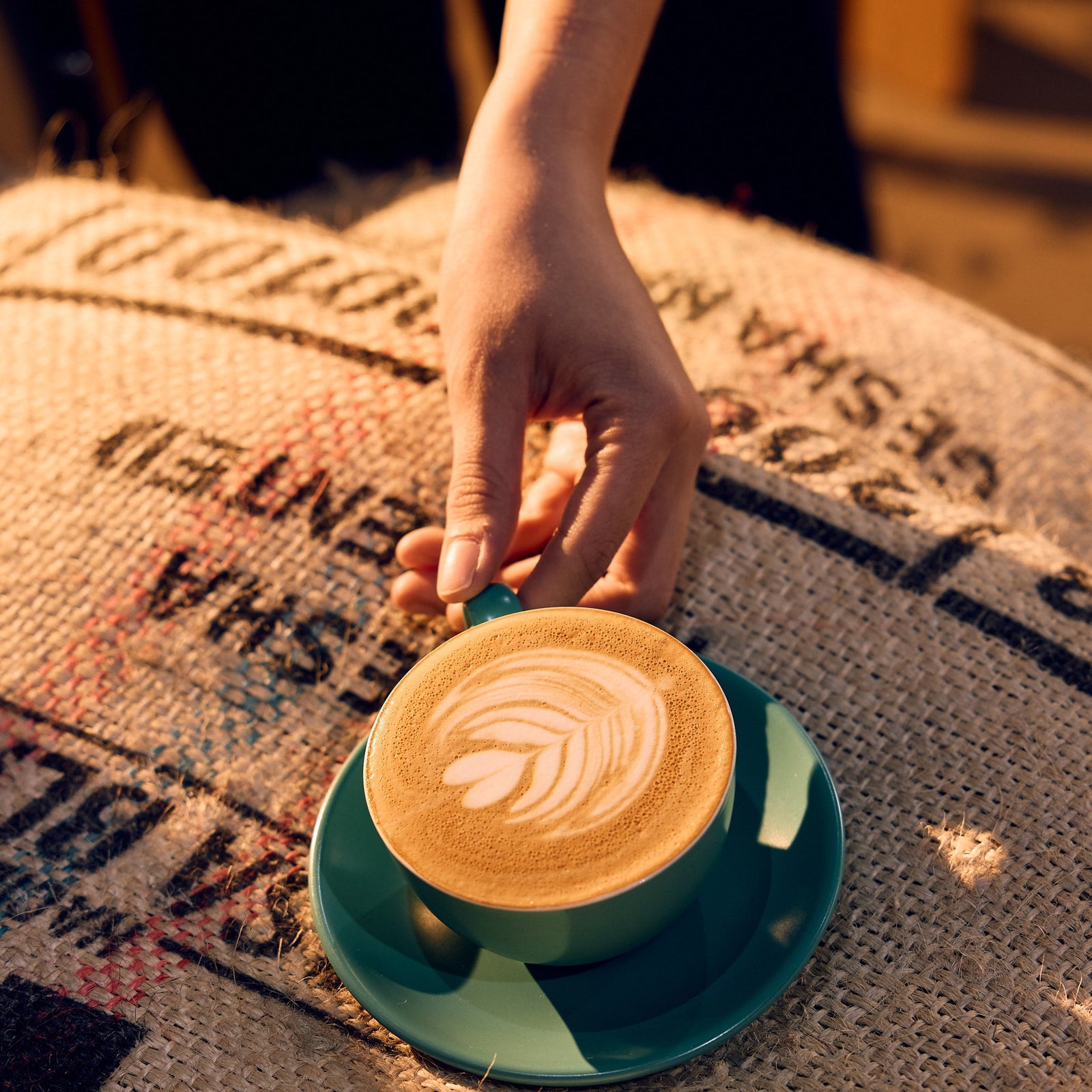 Hand holding a Cafetal coffee cup with a latte art design on a jute coffee bag